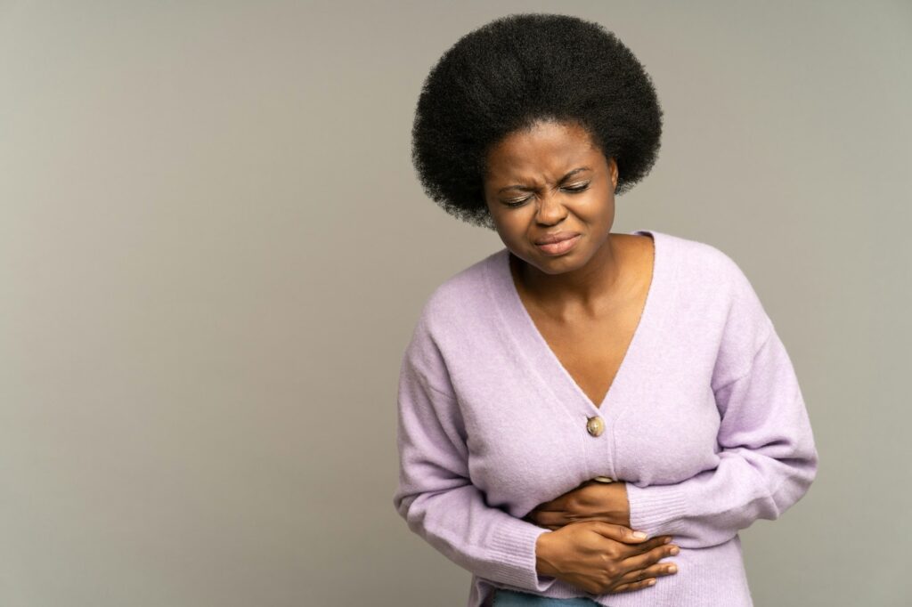 Sick african woman suffer acute period pain or ache in stomach pressing hands to abdominal belly